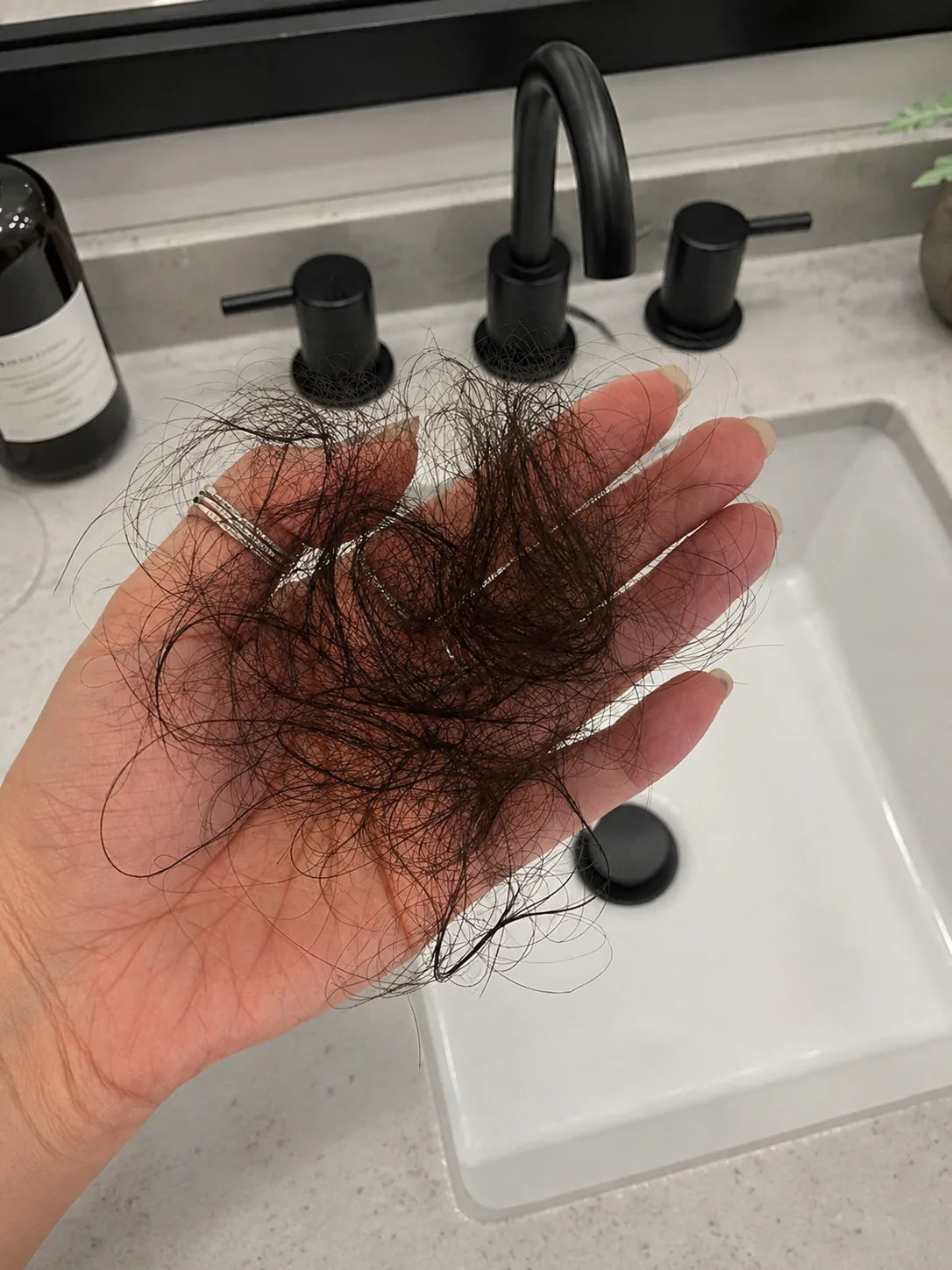 Hand holding loose hair strands over a bathroom sink